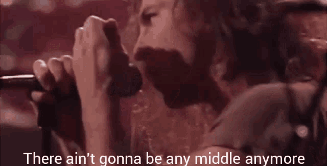 a man singing into a microphone with the words " there ain 't gonna be any middle anymore " next to him