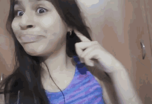 a woman in a blue tank top is making a funny face with her finger in her ear
