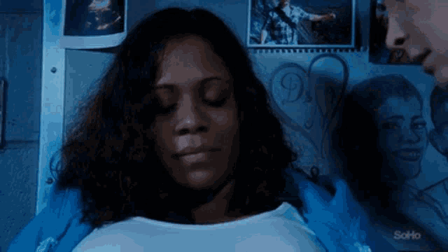 a woman is laying on a bed with her eyes closed in front of a wall with pictures .