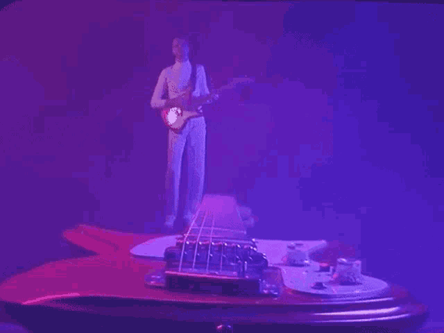 a man is playing a guitar in a dark room with a purple light behind him .