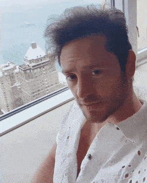 a man in a white shirt looks out a window