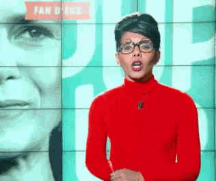 a woman in a red turtleneck and glasses stands in front of a fan d' eve sign