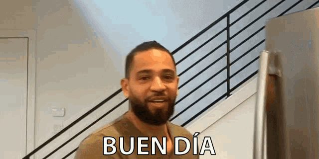 a man with a beard is standing in front of a refrigerator and saying bueno