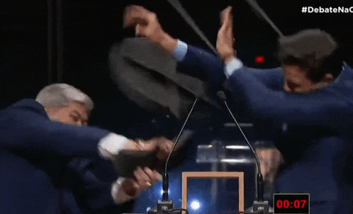 a man giving another man a high five in front of a microphone and a sign that says " debatenac "
