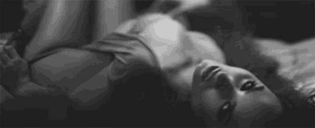 a black and white photo of a woman in lingerie laying on a bed .