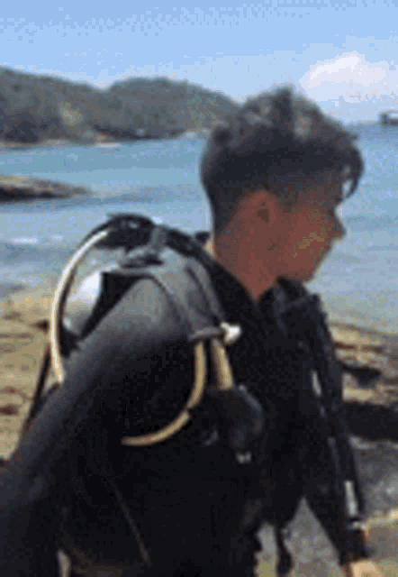 a man in a scuba diving suit is standing on a rock near the water .