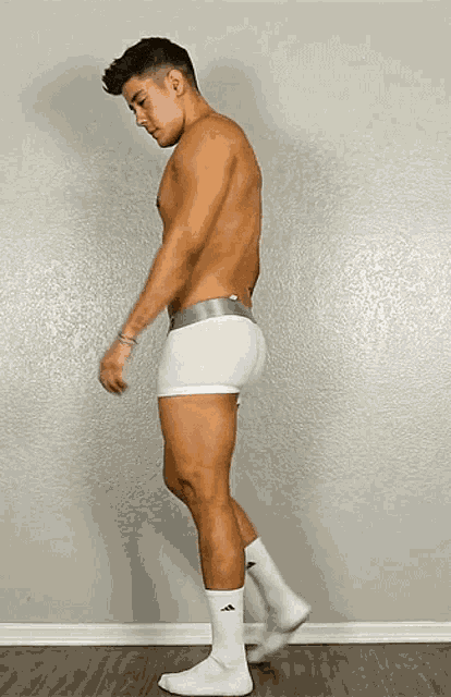 a shirtless man in white boxer shorts and white socks is standing in front of a wall .