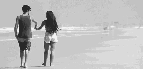 a black and white photo of a man and a woman walking on the beach .