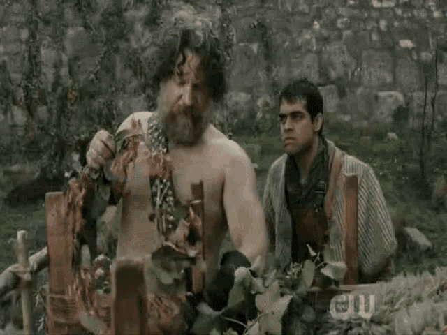 a man without a shirt is standing in a field with a sign that says cw on it