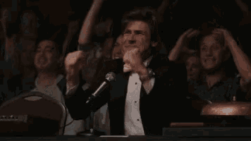 a man in a tuxedo is standing in front of a microphone in front of a crowd .