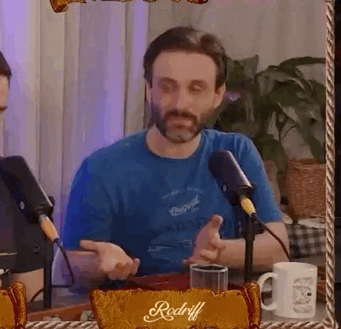 a man with a beard is sitting in front of a microphone and talking .