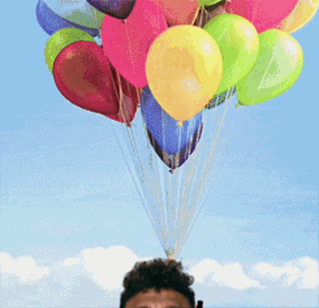 a bunch of colorful balloons are hanging from a string over a man 's head