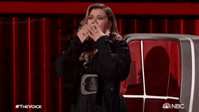 a woman is sitting in front of a red curtain and covering her face with her hands .