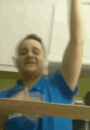a man in a blue shirt holds up his arm in the air