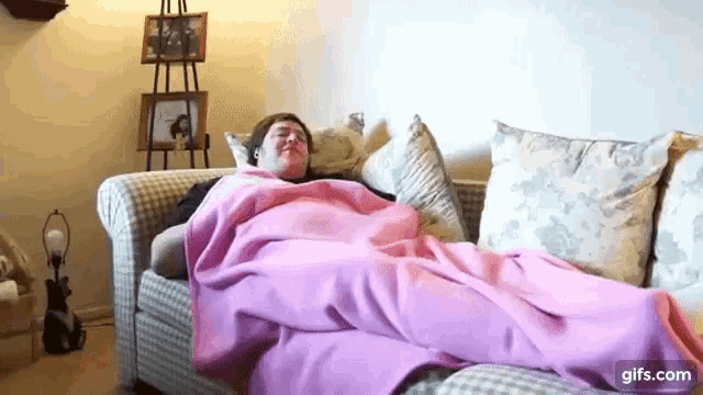 a woman is laying on a couch with a pink blanket on her .
