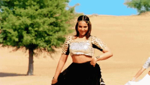 a woman is dancing in the desert wearing a crop top and skirt .