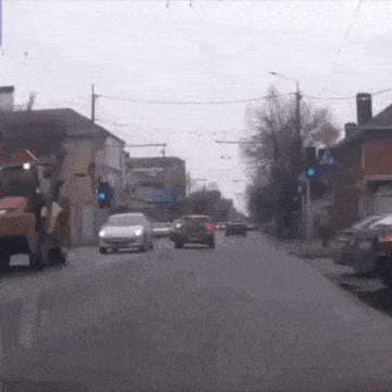 a white car is driving down a street next to a yellow tractor .