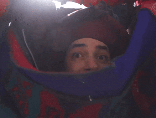 a man with a beard wearing a red hat looks out of a bag