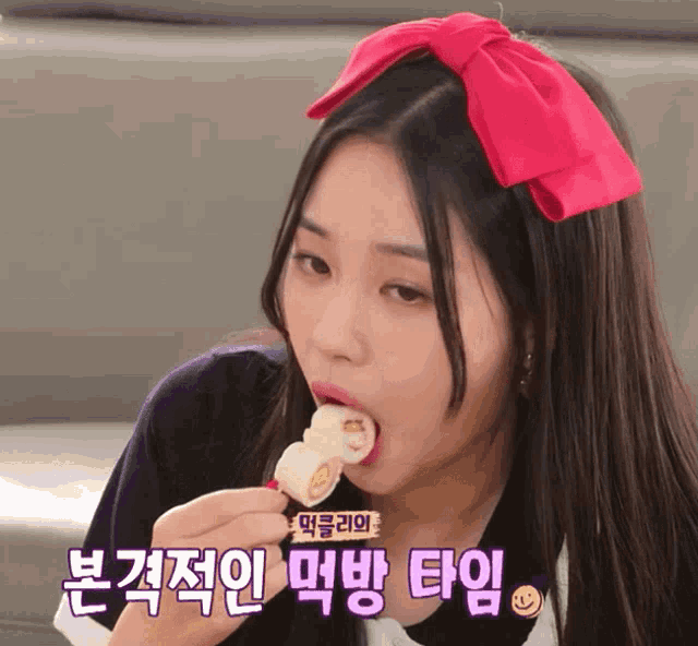 a girl with a red bow on her head is eating a piece of food