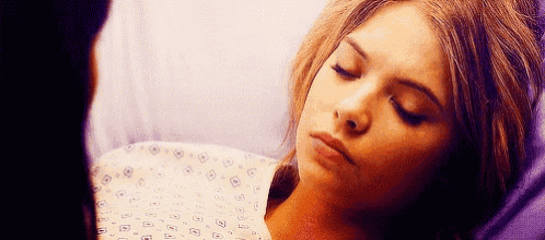 a woman is laying in a hospital bed with her eyes closed and a man standing next to her .