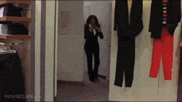 a woman in a suit is standing in a dressing room with movieclips.com on the bottom right