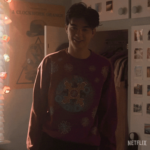 a clockwork orange poster hangs on a wall behind a man wearing a sweater