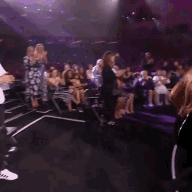 a woman in a black dress is dancing on stage in front of a crowd .