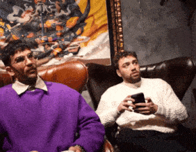 a man in a purple sweater sits next to another man in a chair