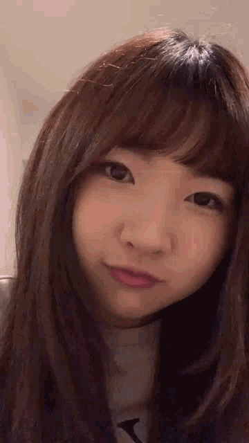 a close up of a woman 's face with long brown hair and bangs .