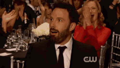 a man in a suit and tie is sitting in front of a crowd with a cw logo on the bottom