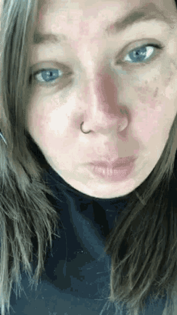 a close up of a woman 's face with blue eyes and a nose ring