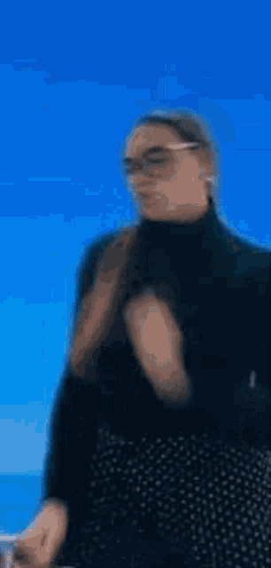 a woman wearing a black turtleneck and polka dot skirt is standing in front of a blue background .
