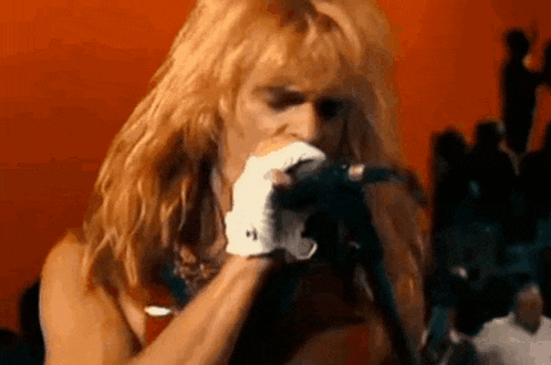 a man with blonde hair is singing into a microphone while wearing white gloves .