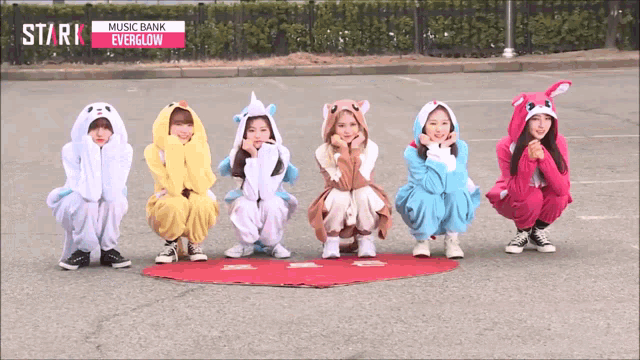 a group of girls are squatting down in front of a music bank everglow sign