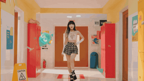 a girl in a plaid skirt is walking down a hallway with a caution sign