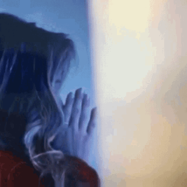 a woman is standing in front of a window with her hands on the glass .