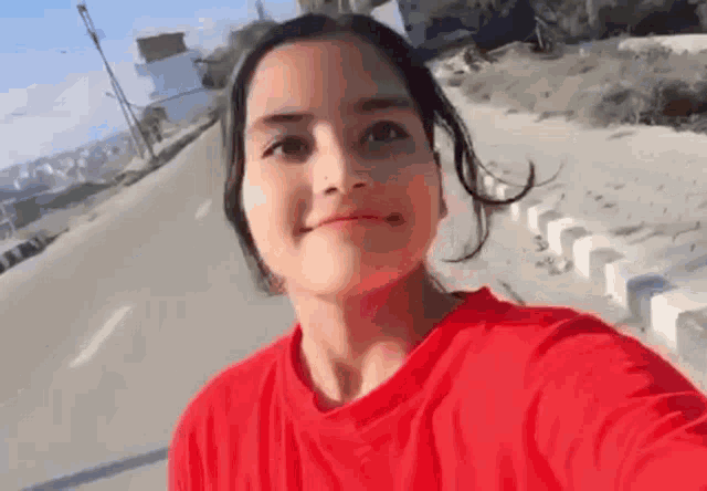 a woman in a red t-shirt is taking a selfie on the side of a road .