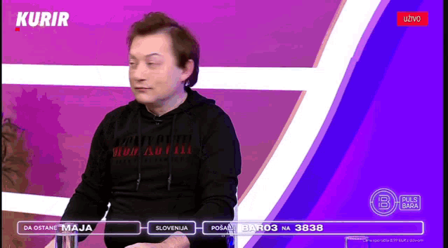 a man in a black hoodie is sitting in front of a purple background that says kurir on it