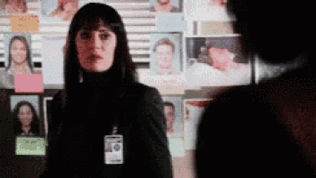a woman with a name tag on her neck is standing in front of a wall with pictures on it .