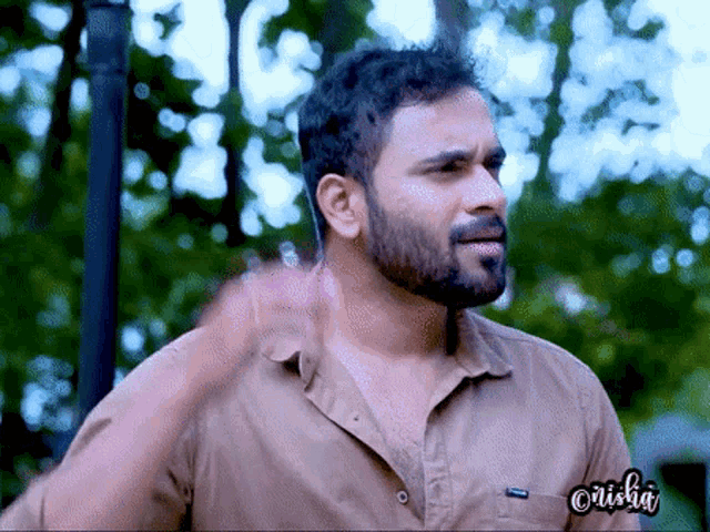 a man with a beard is wearing a brown shirt with the name crisha on the front