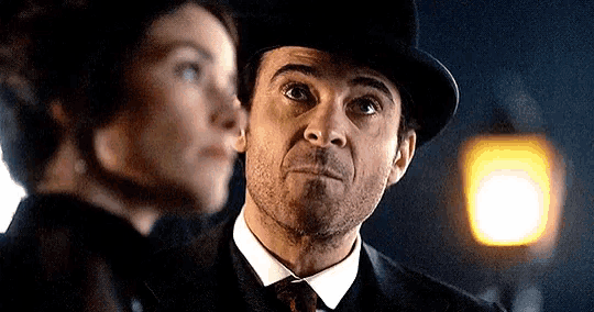 a man in a top hat is standing next to a woman in a suit .