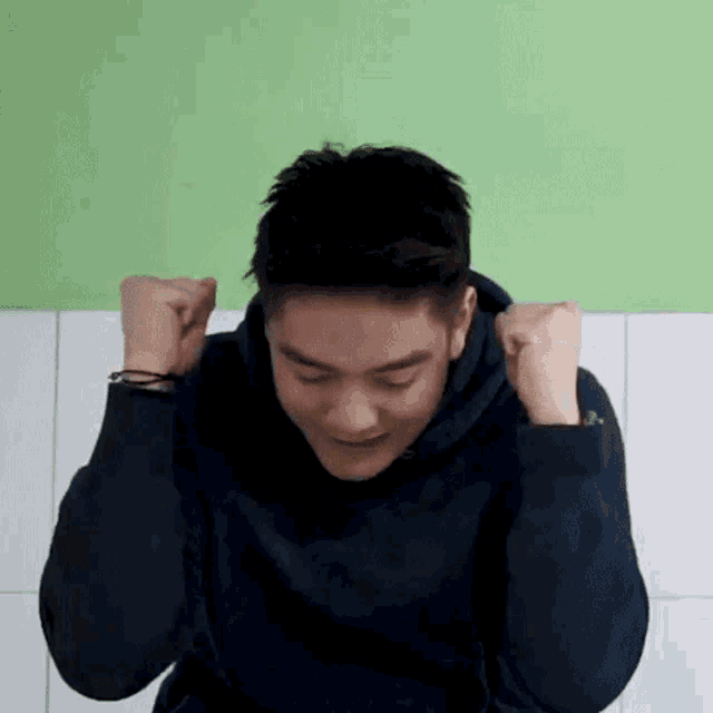 a man in a black hoodie is holding his fists in the air .