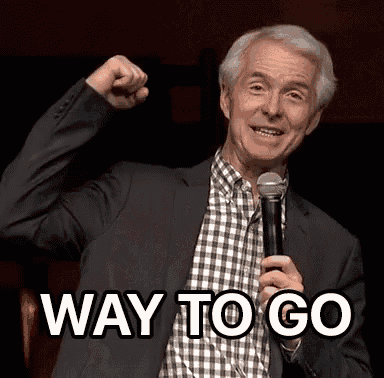 a man in a suit and plaid shirt is holding a microphone and saying way to go