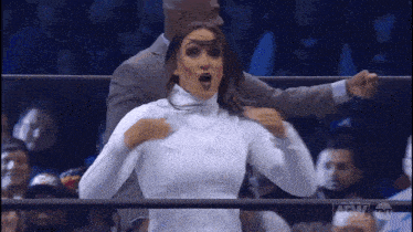 a woman in a white turtleneck is standing in a ring with a man in a suit .
