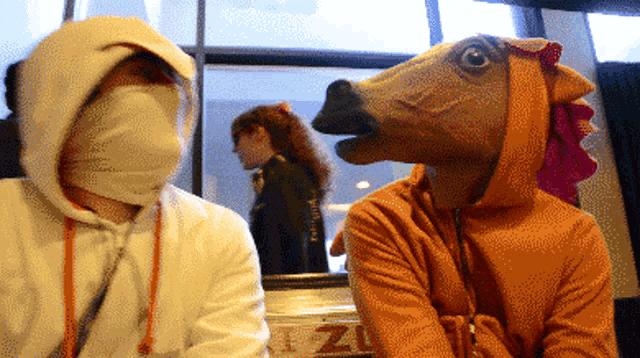 a man wearing a horse mask sits next to another man wearing a chicken mask