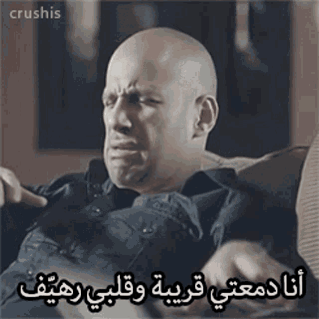 a bald man is sitting on a couch with arabic writing on the bottom
