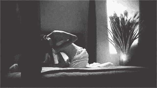 a black and white photo of a woman laying on a bed next to a window .