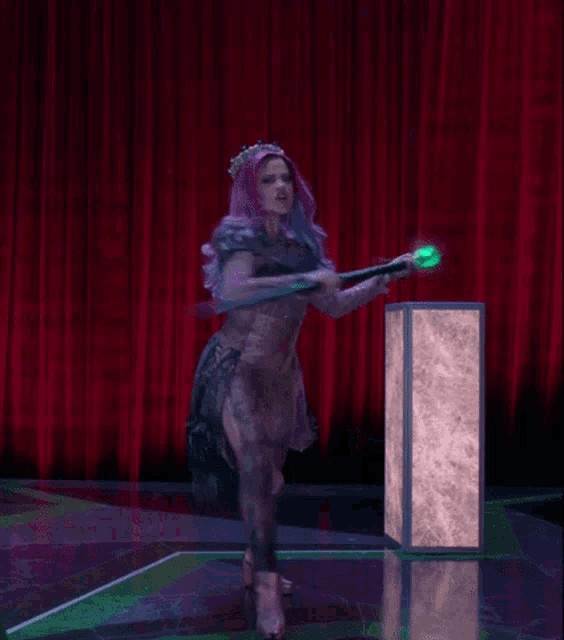 a woman with purple hair is standing in front of a red curtain and holding a green object .