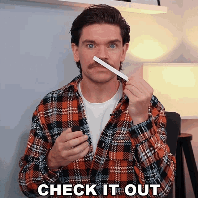 a man in a plaid shirt is holding a piece of paper in front of his nose and the words check it out below him