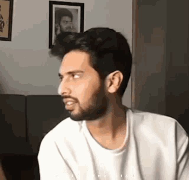a man with a beard is wearing a white t-shirt and looking to the side .